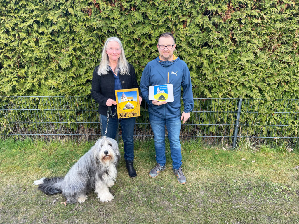 Ina Baumbach mit ihrem Hund Floyd und Woltersdorfs Bürgermeister Tobias Gauster mit den offiziellen Wappen von Woltersdorf.