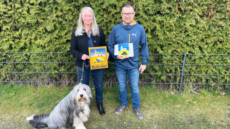 Ina Baumbach mit ihrem Hund Floyd und Woltersdorfs Bürgermeister Tobias Gauster mit den offiziellen Wappen von Woltersdorf.