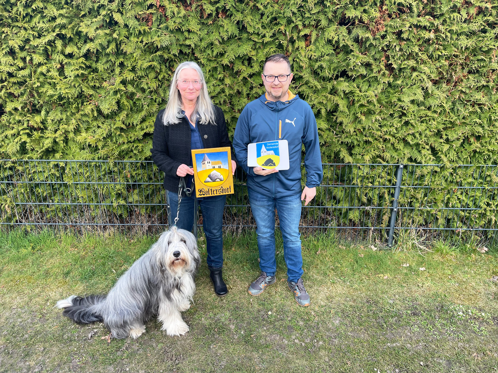 Ina Baumbach mit ihrem Hund Floyd und Woltersdorfs Bürgermeister Tobias Gauster mit den offiziellen Wappen von Woltersdorf.