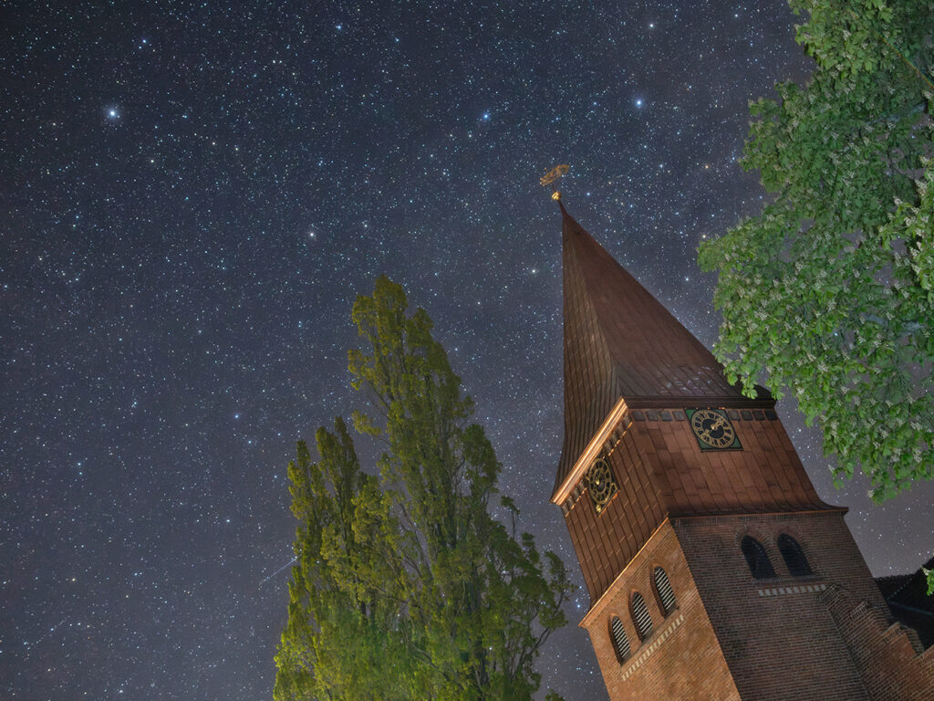 nach aufwendiger Renovierung erstrahlt die Michaeliskirche von Schnega
jetzt wieder in neuem Glanz.  Meine Aufnahme ist gestern Morgen um 02:12 Uhr entstanden. Links oben
ist der Polarstern zu sehen. Das Sternbild Cepheus erstreckt sich über
den gesamten übrigen Himmelsbereich. Schon bei mittlerer Bildschirmgröße
ist rechts am Kastanienlaub Herschels Granatstern mit seinem auffällig
rötlichen Schimmer erkennbar.
