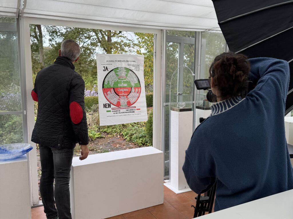 Anaisio Guedes (links) von "Bares für Rares" fotografiert in Groß Heide während der Sendung die von Sybille Homann gestaltete Vitrine mit dem Kunstwerk von Joseph Beuys. Foto: S. Homann